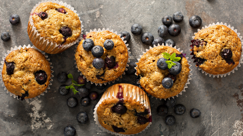 Ansicht von oben auf einen Tisch voller Blaubeermuffins und verstreuter Beeren