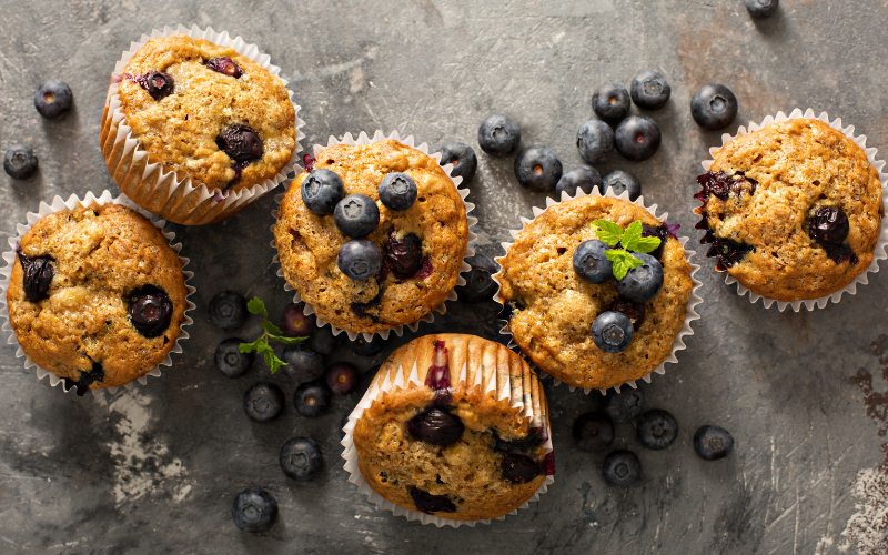 Ansicht von oben auf einen Tisch voller Blaubeermuffins und verstreuter Beeren