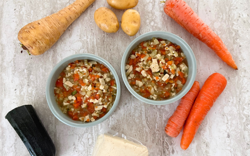Draufsicht der fertigen Suppe in Futternöpfen mit den Gemüsezutaten drum herum liegend